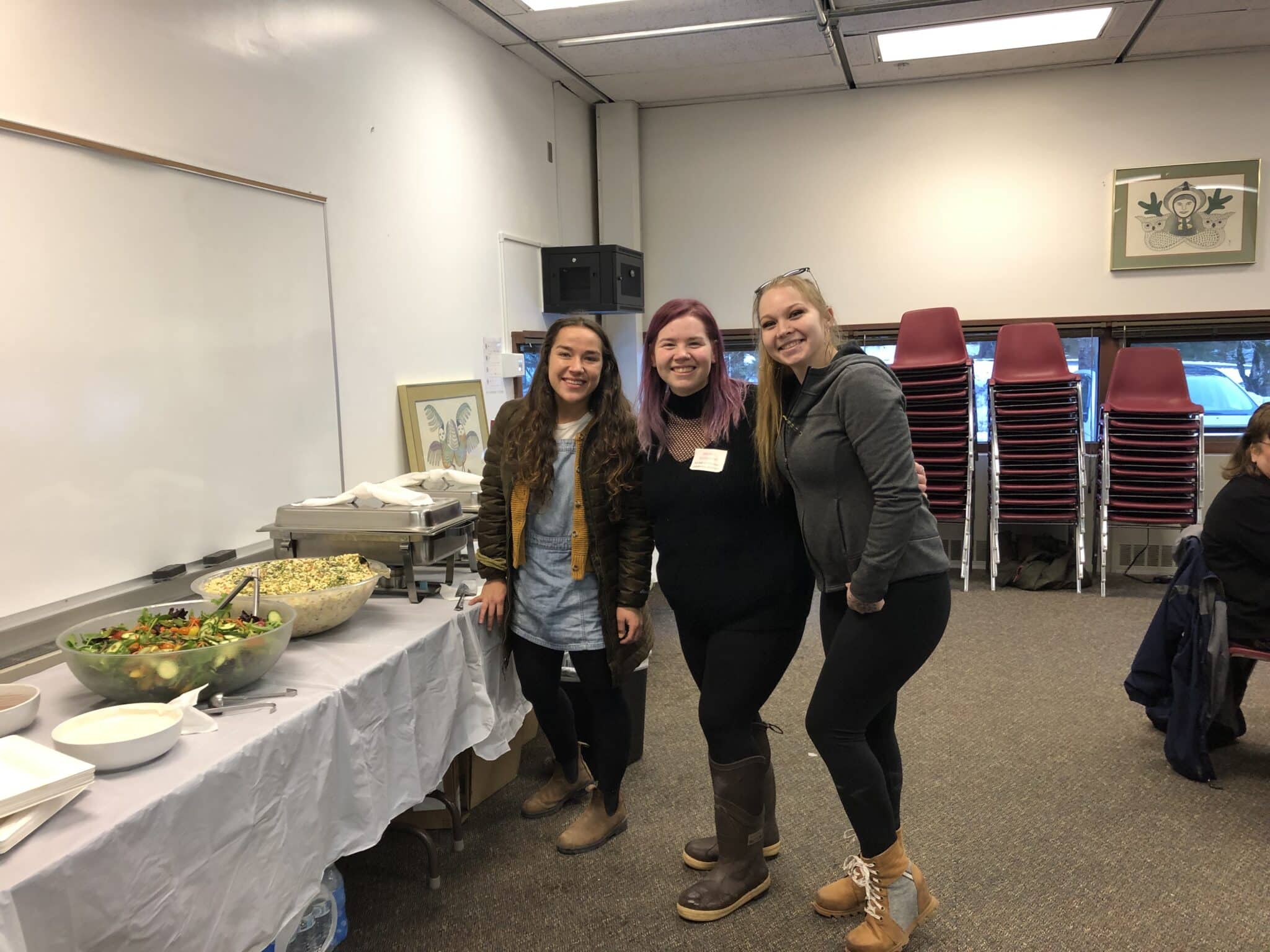Three ladies pose in front of a buffet of food